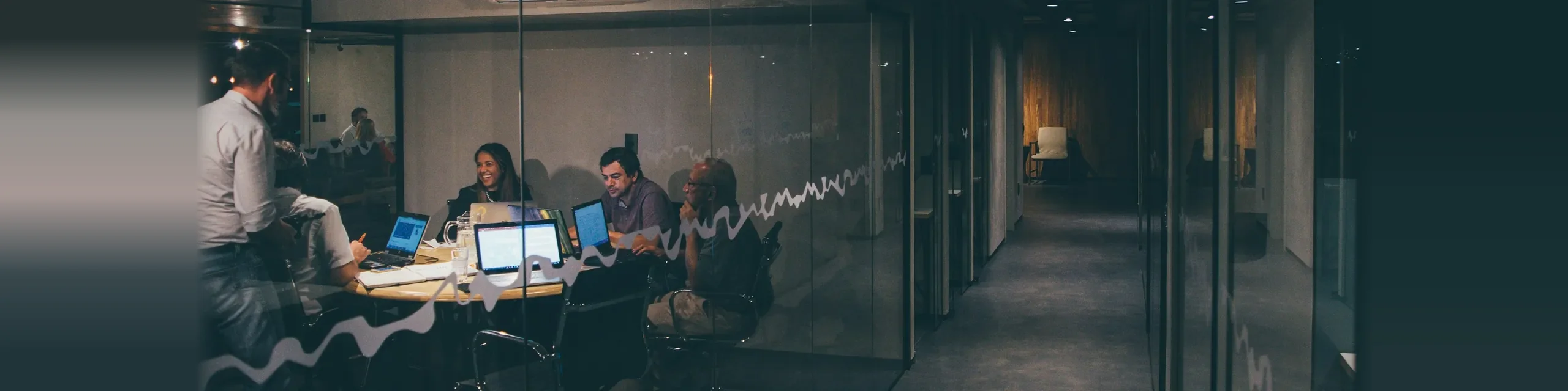 Implementation team working together on laptops in a glass meeting room