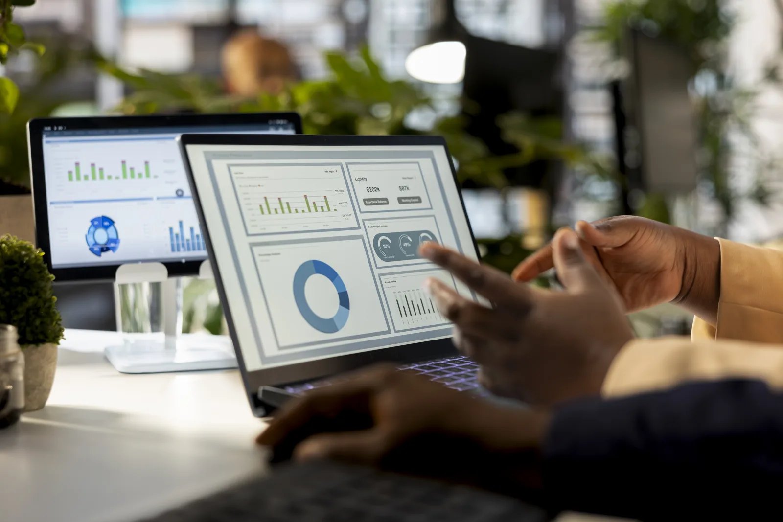 Hands pointing at business dashboards on a laptop and monitor